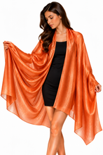 Load image into Gallery viewer, A woman modeling a shimmering metallic orange wrap or shawl draped over a black dress against a plain white background.