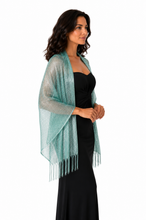Load image into Gallery viewer, A woman wearing a shimmering turquoise green open-knit shawl with fringe over a black dress, shown against a plain white background.