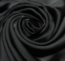 Load image into Gallery viewer, A close-up of draped black fabric arranged in a spiral rose pattern, showing a smooth satin-like sheen and soft folds.