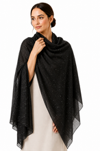 Load image into Gallery viewer, A woman modeling a black sheer shawl with subtle silver glitter speckles, draped over her shoulders and arms over a light-colored dress against a plain white background.