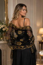 Load image into Gallery viewer, A woman wearing a black off-the-shoulder evening gown with elaborate gold floral embroidery and sheer embroidered sleeves, photographed in an elegant indoor setting.