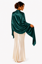 Load image into Gallery viewer, A woman shown from the back wearing a dark green satin  pashmina shawl draped wrap or shawl over a cream satin maxi dress, set against a plain white studio background.